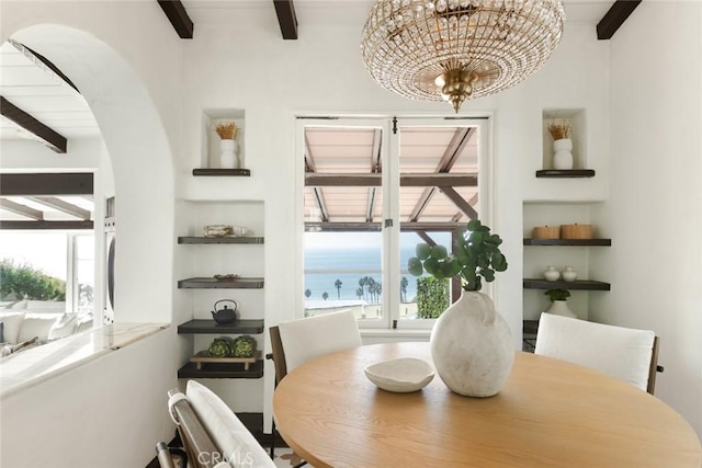 dining room featuring beamed ceiling, a healthy amount of sunlight, a water view, and a chandelier