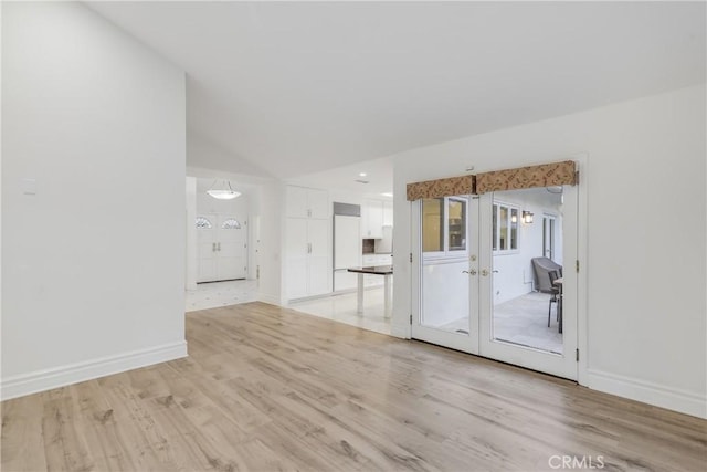 spare room featuring light wood-type flooring, french doors, and vaulted ceiling