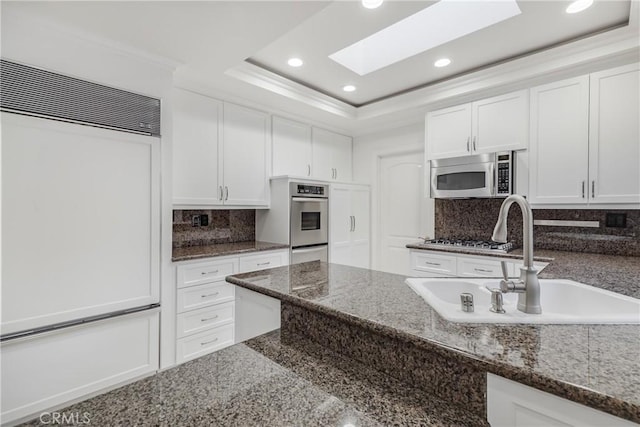 kitchen featuring a skylight, sink, dark stone counters, white cabinets, and appliances with stainless steel finishes