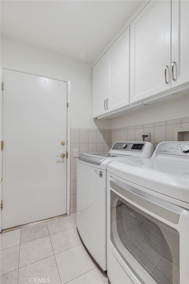 clothes washing area with washer and clothes dryer, cabinets, light tile patterned floors, and tile walls