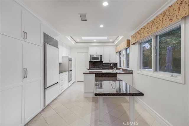 kitchen featuring paneled built in fridge, sink, a skylight, a tray ceiling, and white cabinetry