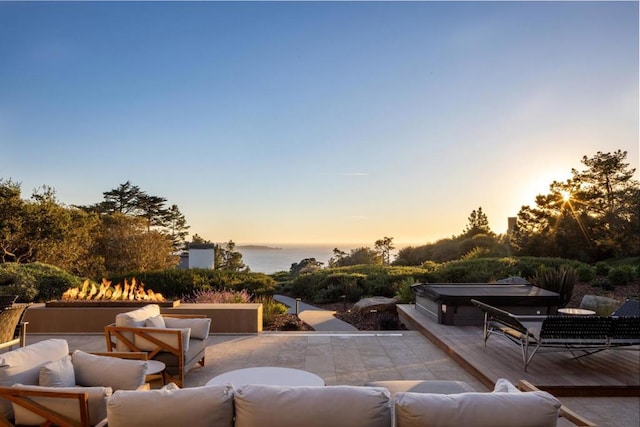 patio terrace at dusk with a water view, a hot tub, and an outdoor hangout area