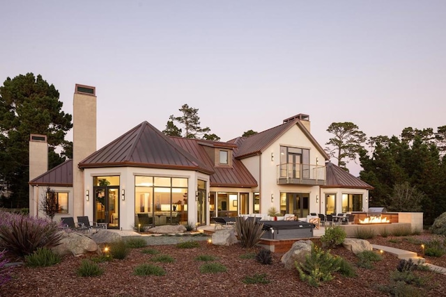 back house at dusk featuring a balcony, a hot tub, an outdoor fire pit, and a patio area