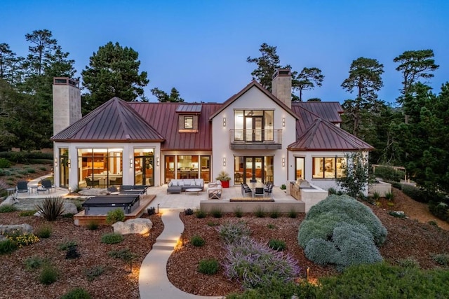 back house at dusk with a patio area, an outdoor living space, a balcony, and a hot tub