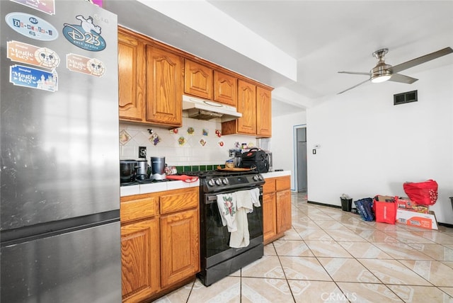 kitchen featuring backsplash, black stove, ceiling fan, light tile patterned floors, and stainless steel refrigerator