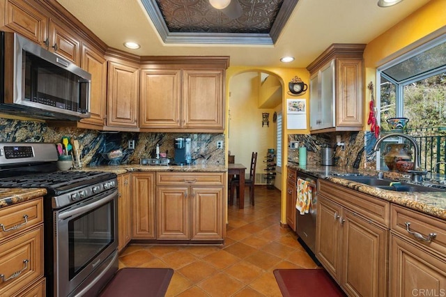 kitchen with backsplash, ornamental molding, stainless steel appliances, a tray ceiling, and sink