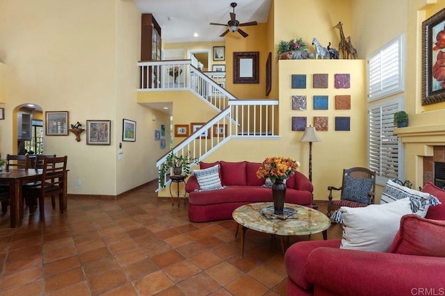 tiled living room featuring ceiling fan, a high ceiling, and a tiled fireplace