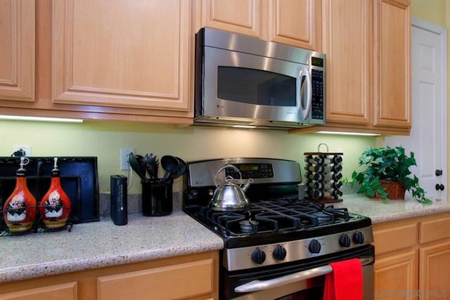 kitchen featuring light brown cabinets, stainless steel appliances, and light stone counters