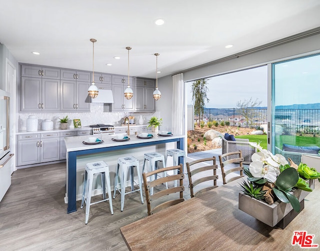 kitchen featuring gray cabinetry, premium range hood, backsplash, hanging light fixtures, and hardwood / wood-style flooring