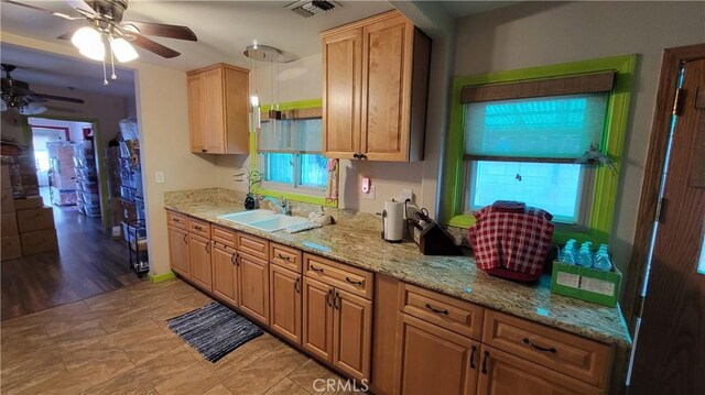 kitchen with ceiling fan, light stone countertops, and sink