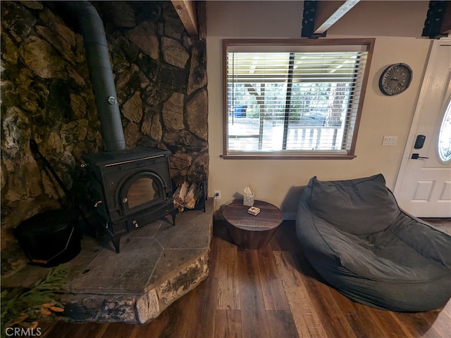 sitting room featuring wood-type flooring, a wood stove, and beamed ceiling