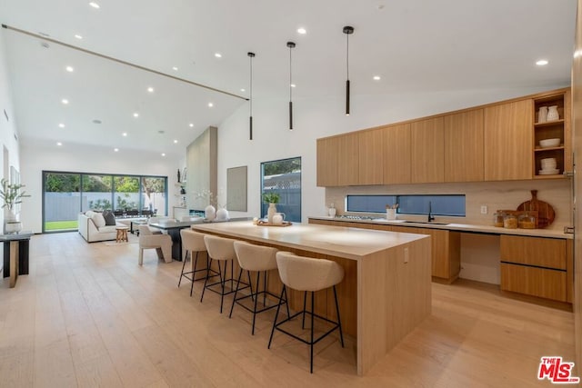 kitchen featuring tasteful backsplash, a spacious island, hanging light fixtures, high vaulted ceiling, and light hardwood / wood-style flooring