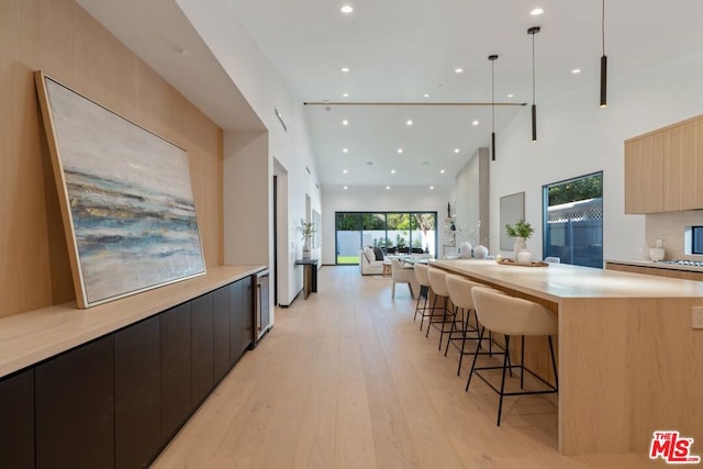 kitchen featuring light brown cabinetry, decorative light fixtures, light wood-type flooring, a high ceiling, and a kitchen island