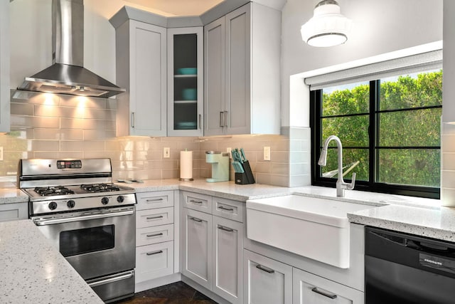 kitchen featuring wall chimney exhaust hood, black dishwasher, light stone counters, and stainless steel gas range