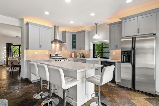 kitchen featuring appliances with stainless steel finishes, wall chimney exhaust hood, a healthy amount of sunlight, and decorative light fixtures