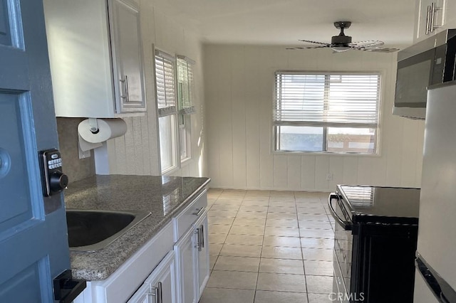 kitchen featuring ceiling fan, sink, light tile patterned floors, white cabinetry, and black / electric stove