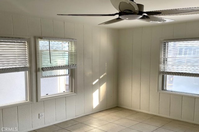 tiled empty room featuring a wealth of natural light, wooden walls, and ceiling fan