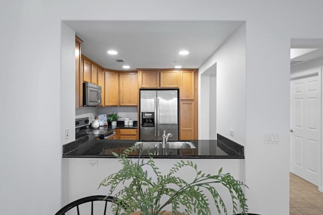 kitchen with dark stone countertops, kitchen peninsula, sink, appliances with stainless steel finishes, and light tile patterned floors