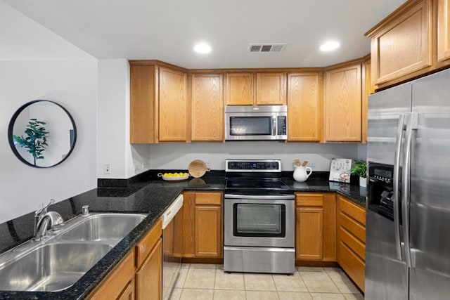 kitchen with light tile patterned floors, dark stone counters, sink, and stainless steel appliances