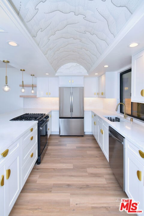 kitchen with pendant lighting, white cabinets, sink, light hardwood / wood-style floors, and stainless steel appliances