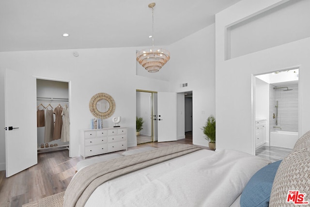 bedroom featuring wood-type flooring, high vaulted ceiling, ensuite bath, and a notable chandelier