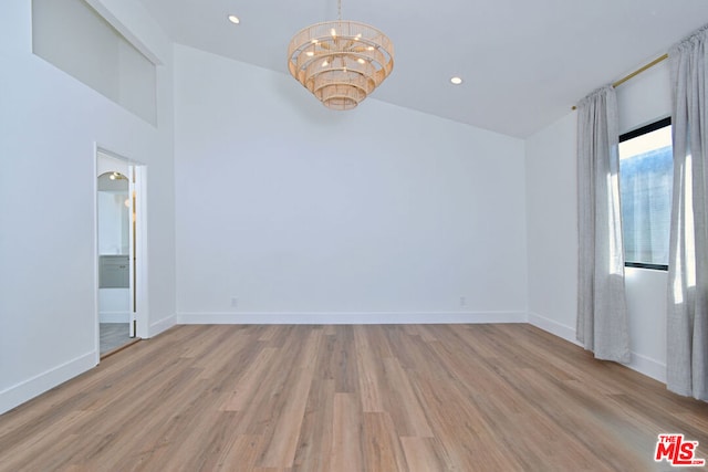 empty room featuring high vaulted ceiling, a chandelier, and light wood-type flooring