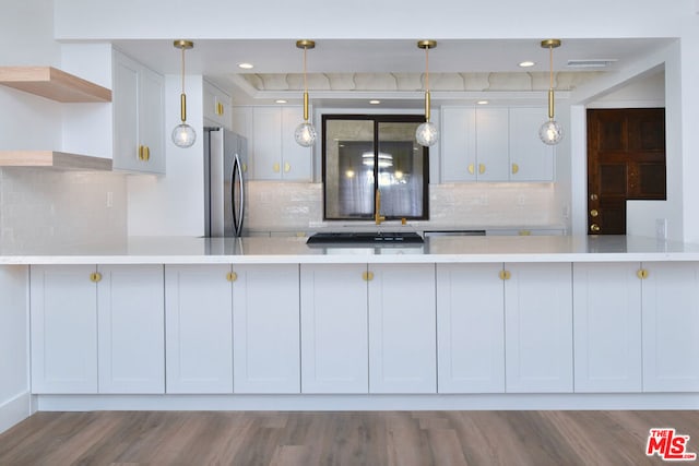 kitchen with kitchen peninsula, stainless steel fridge, decorative backsplash, white cabinets, and hardwood / wood-style flooring