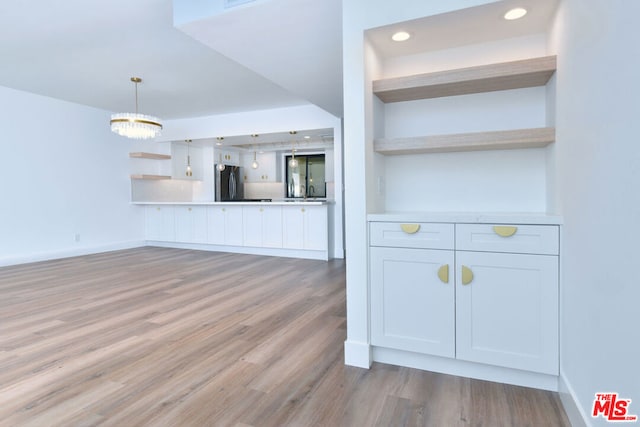 kitchen featuring white cabinets, hanging light fixtures, light hardwood / wood-style flooring, a notable chandelier, and stainless steel refrigerator