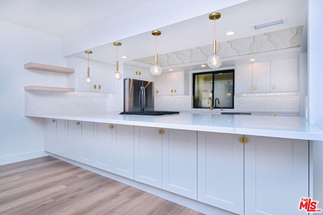 kitchen with stainless steel refrigerator, white cabinetry, hanging light fixtures, and light wood-type flooring