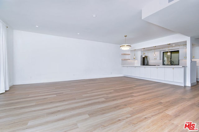 unfurnished living room featuring sink, light hardwood / wood-style flooring, and an inviting chandelier