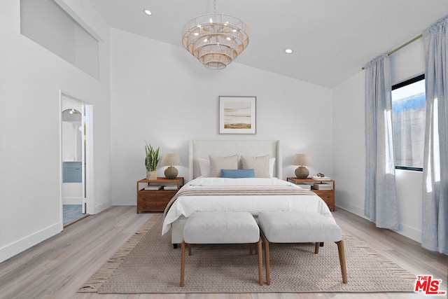 bedroom with a chandelier, light hardwood / wood-style flooring, vaulted ceiling, and ensuite bathroom