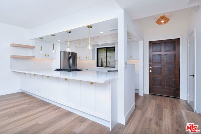 kitchen featuring white cabinets, decorative light fixtures, light hardwood / wood-style floors, kitchen peninsula, and stainless steel refrigerator