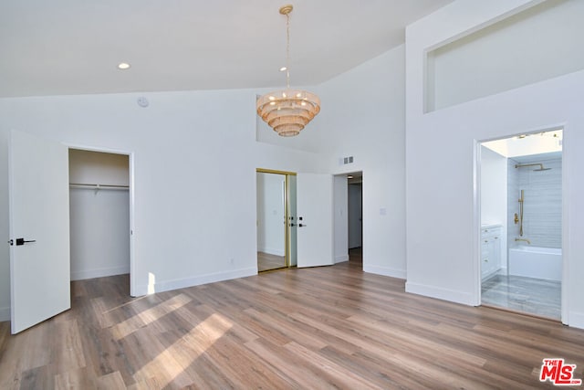 unfurnished bedroom with connected bathroom, hardwood / wood-style floors, and high vaulted ceiling