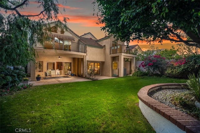 back house at dusk featuring a lawn, a balcony, and a patio