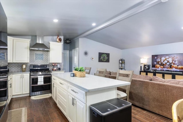 kitchen with wall chimney exhaust hood, stainless steel stove, a kitchen island, dark hardwood / wood-style flooring, and white cabinets