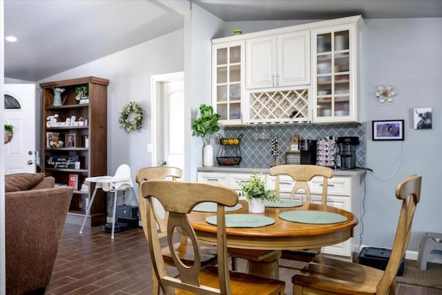 dining space featuring dark hardwood / wood-style flooring, vaulted ceiling, and bar