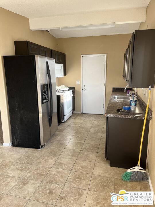 kitchen with light tile patterned flooring, beamed ceiling, sink, white appliances, and dark brown cabinetry