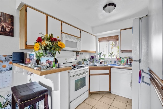 kitchen with a kitchen breakfast bar, sink, light tile patterned floors, white cabinetry, and white appliances