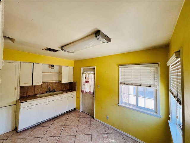 kitchen with light tile patterned flooring, white cabinetry, sink, and backsplash