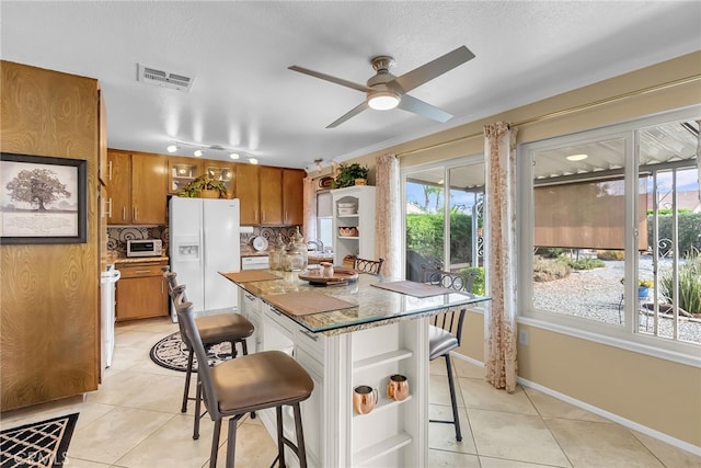 26725 Farrell St, Menifee, CA 92586 - kitchen with white fridge with ice dispenser, brown cabinets, a breakfast bar, light tile patterned floors, and open shelves