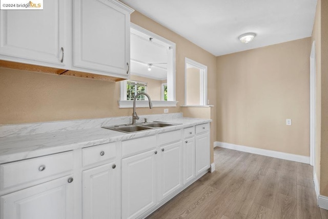 kitchen featuring white cabinets, light stone countertops, sink, and light hardwood / wood-style flooring