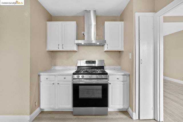 kitchen with wall chimney exhaust hood, white cabinetry, and stainless steel range with gas stovetop