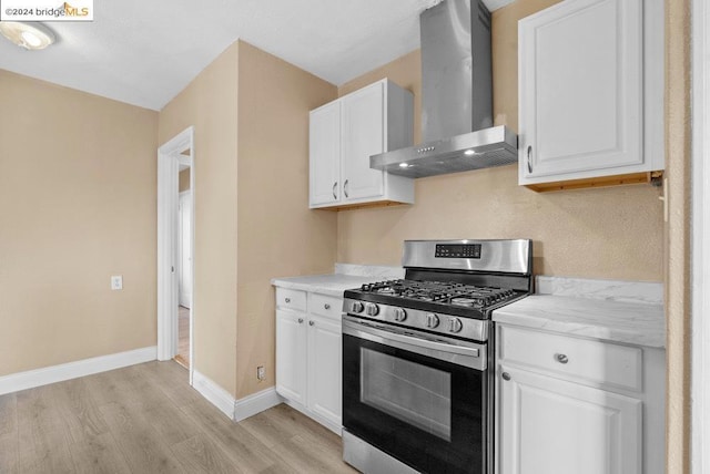 kitchen with wall chimney exhaust hood, white cabinetry, light hardwood / wood-style flooring, and stainless steel range with gas stovetop