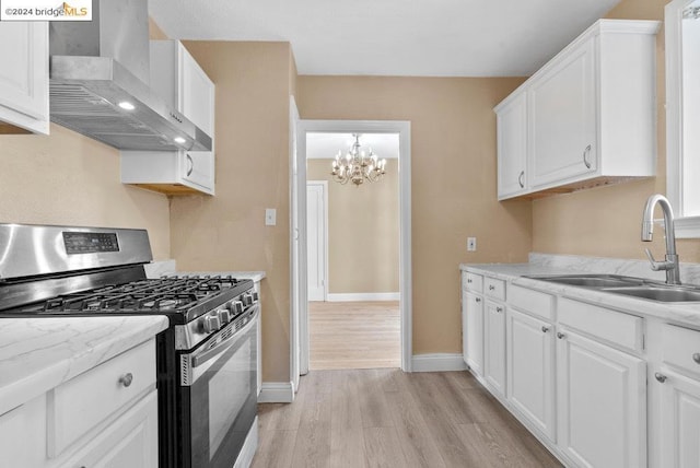 kitchen featuring sink, wall chimney range hood, stainless steel range with gas cooktop, white cabinets, and light wood-type flooring