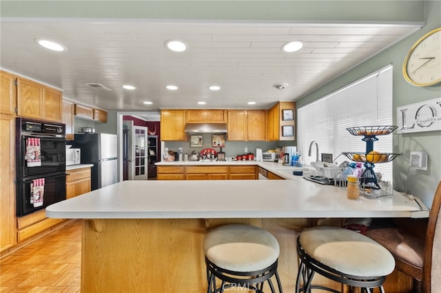 kitchen featuring light parquet flooring, kitchen peninsula, stainless steel fridge, a breakfast bar area, and black double oven