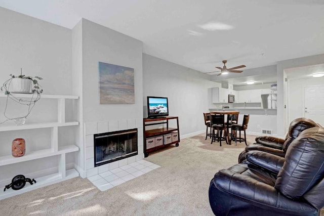 living room with ceiling fan, light carpet, a fireplace, and built in shelves