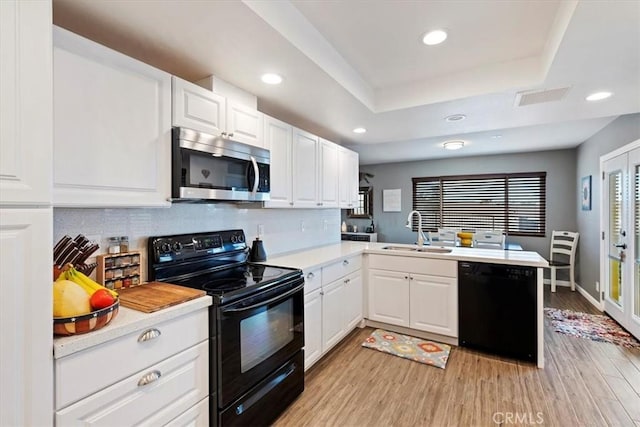 kitchen featuring kitchen peninsula, a tray ceiling, black appliances, white cabinets, and sink