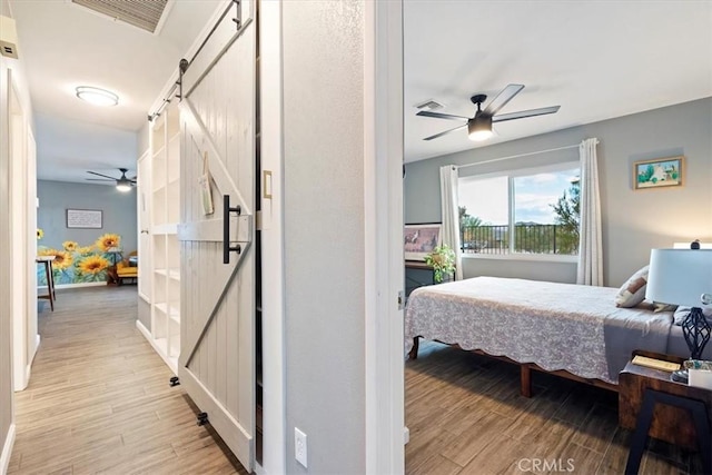 bedroom featuring ceiling fan, a barn door, and light hardwood / wood-style floors