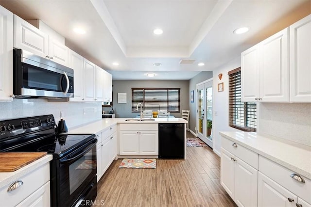 kitchen with white cabinets, black appliances, sink, a raised ceiling, and light wood-type flooring