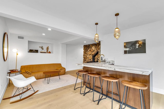 bar featuring light stone counters, decorative light fixtures, and light wood-type flooring